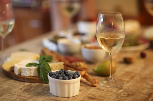 Wooden table set with white wine and assorted delicious snack of cheese and olives in living room in the evening
