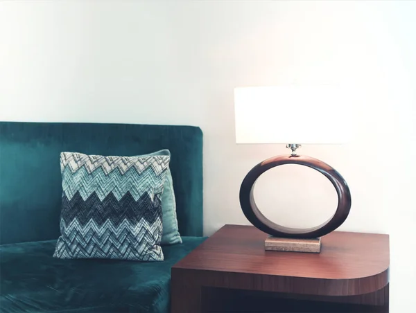 白壁のモダンなアパートでクッションと居心地の良い緑のソファの近くに配置されたランプとエレガントな木製のテーブル — ストック写真