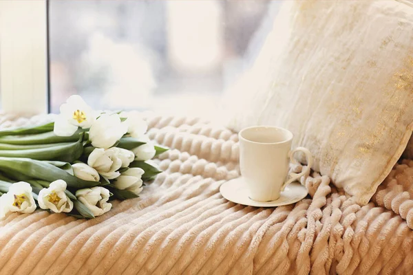 一束新鲜的白色郁金香和一杯白咖啡放在舒适的床上 床上铺着米黄色的毛毯和睡在轻便的卧室里的枕头 — 图库照片