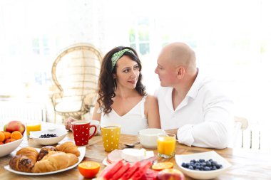 Beyazlar içindeki nazik kadın ve adam birbirlerine aşkla bakıyor. Işık odasında oturmuş, kahvaltı sofrasında yemek yiyorlar.