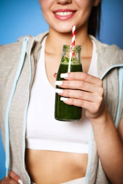 Yeşil smoothie ile ekin memnun genç kadın duvarın arkasında gülüyor