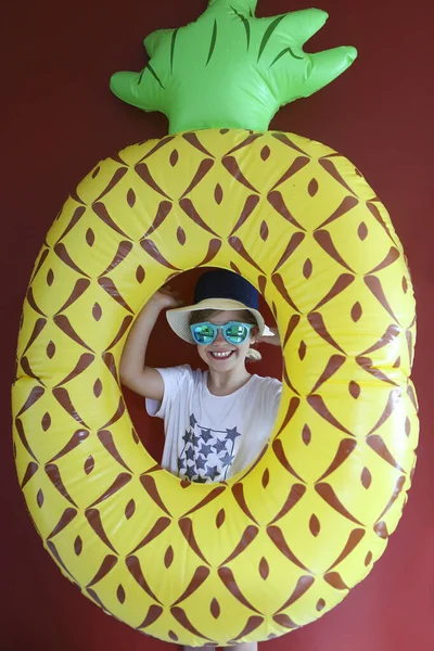 Pretty emothional child wear a hat and sunglasses holding swiming float ready to swimm on a red background. Copy space, daylight