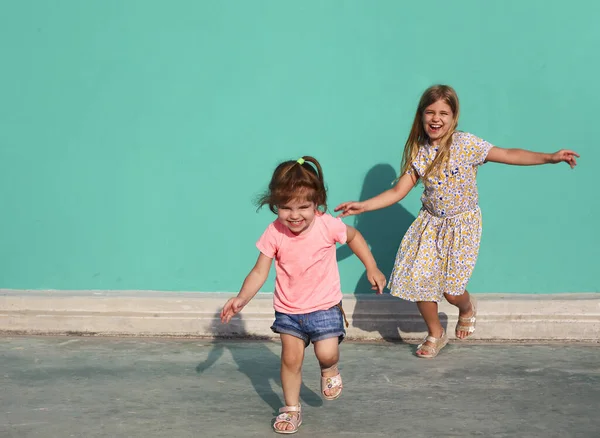 陽気な小さな女の子でカラフルなドレスに対して実行している緑の壁に対して太陽の下で楽しい一緒に — ストック写真