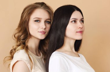 Bej arka planda kamera pozu veren iki güzel çok kültürlü genç kadın.