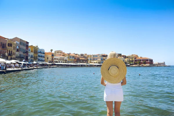 大きな帽子の若いブロンドの女性は ベネチアンスタイルでチャニアの港の美しい景色を楽しんでいます 歴史建築旅行 チャニア クレタ島 ギリシャ — ストック写真