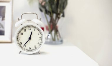 Çerçeveli beyaz çalar saat ve komodinin üzerinde çiçekler 