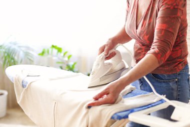 Evdeki rahat ışık odasında ev işlerini yaparken temiz giysileri ütüleyen olgun bir kadın. Kapat şunu.