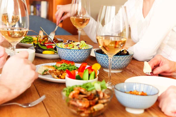 Group of anonymous people eating healthy food and enjoying wine while sitting at table during dinner at home