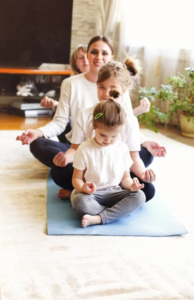 成年妇女和小女孩在家里一起做瑜伽时 排成一列坐在地板上 张开双臂 — 图库照片