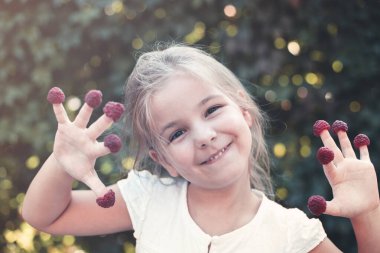 Dışarıda parmaklarında ahududu olan mutlu küçük bir çocuk. 