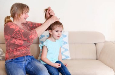 Mutlu olgun bir kadın, sabah evde kanepede otururken gülüyor ve at kuyruğu yapıyor.