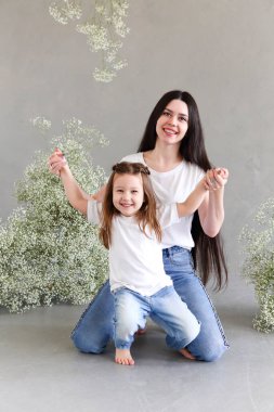 Genç esmer anne ve küçük kızı büyük çiçekli çelenk ile duvarın yanında duruyor. Anneler günü danışmanı.