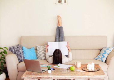 Arka planda, rahat oturma odasındaki projede çalışırken koltukta uzanmış, ayakları havada profesyonel edebiyat okuyan, tanınmamış, çıplak ayaklı genç bir kadın var.