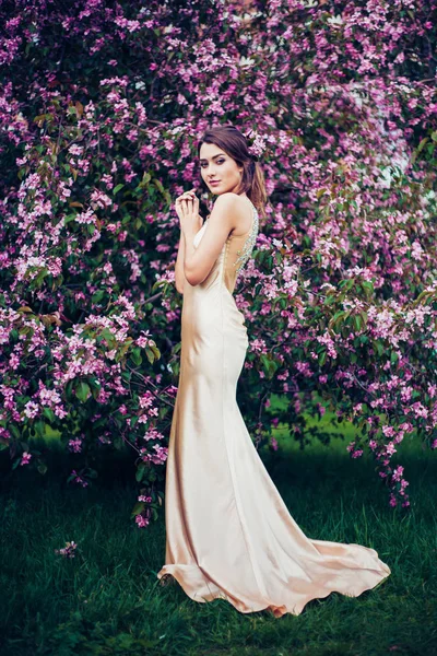 Retrato de una joven mujer hermosa posando entre los árboles de flores de primavera . —  Fotos de Stock