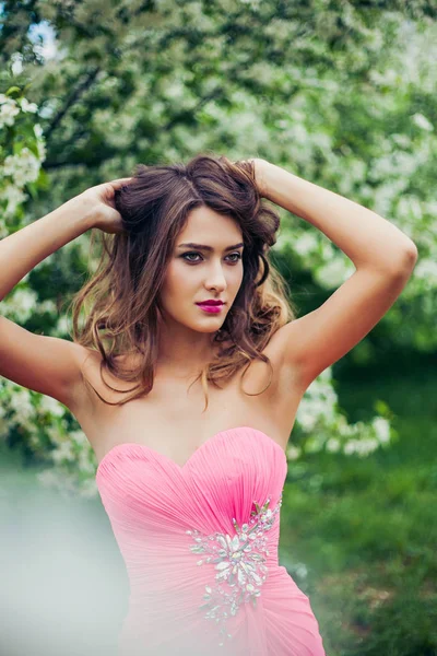 Retrato de una joven mujer hermosa posando entre los árboles de flores de primavera . —  Fotos de Stock