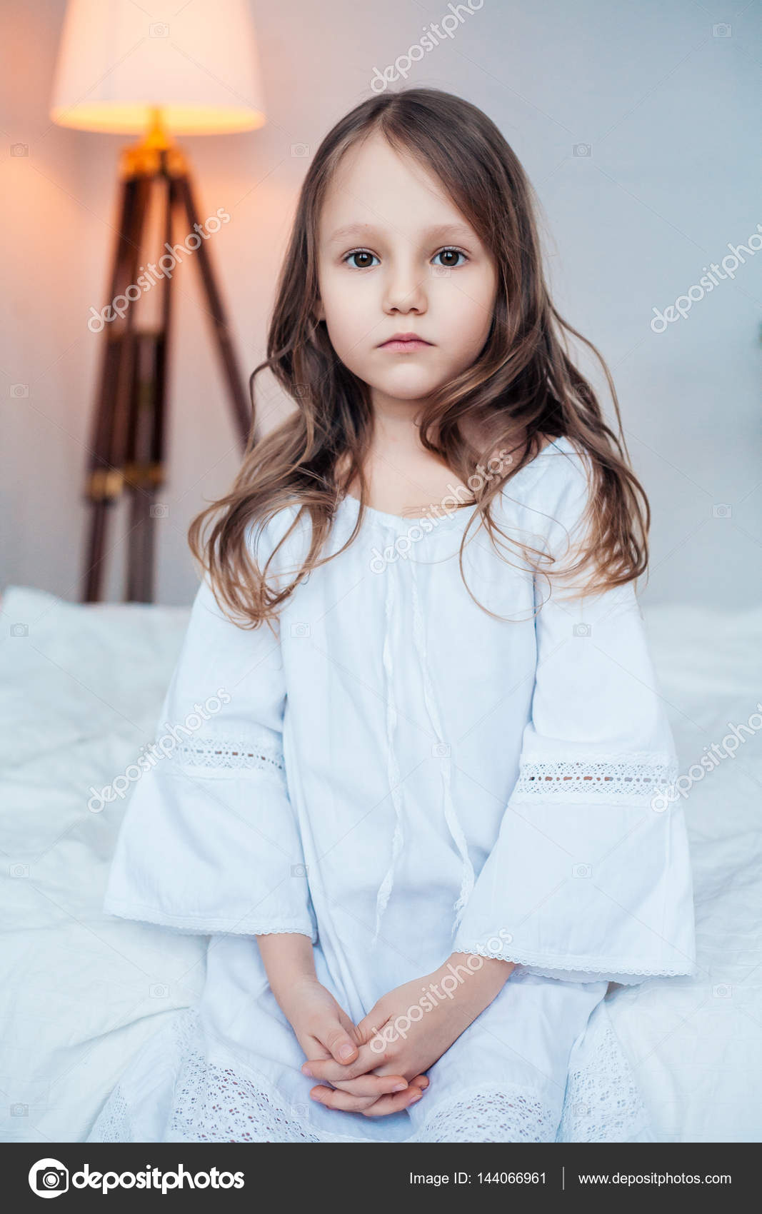 Cute little girl wearing nightgown sitting on the bed. Stock Photo