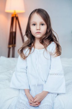 Sevimli küçük kız yatakta oturmuş geceliğini giymiş.