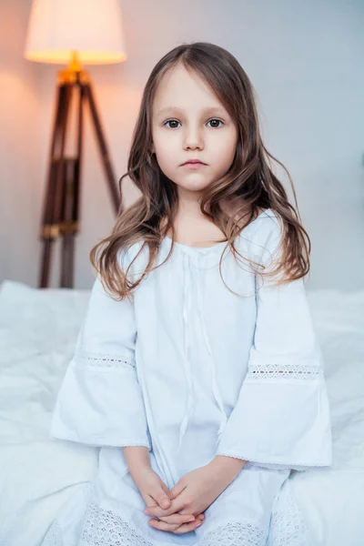 Linda niña con camisón sentado en la cama . —  Fotos de Stock