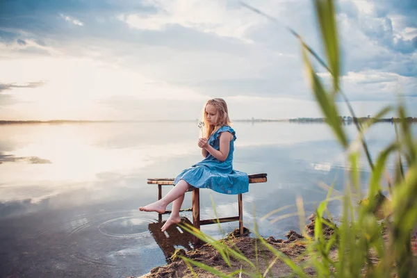 Roztomilé dítě dívka sedící na dřevěné platformě u jezera. — Stock fotografie