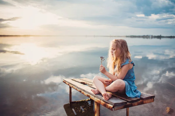 Göl kenarındaki ahşap bir platformda oturan kız şirin çocuk. — Stok fotoğraf