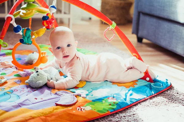 Bambina di 4 mesi sdraiata sul tappeto da gioco colorato sul pavimento. Tappeto attività per bambini. Sviluppo precoce a casa . — Foto Stock