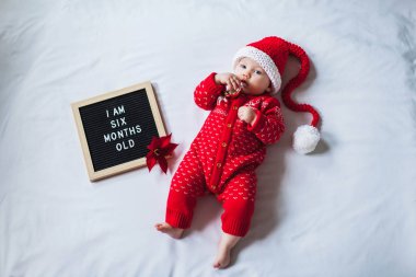 6 aylık bebek beyaz arka plan üzerine uzanmış Noel Baba kostümü giyiyor. Düz konum.