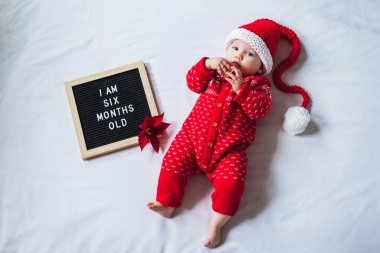6 aylık bebek, beyaz arka plan üzerine uzanmış Noel Baba kostümü giyiyor. Düz konum.