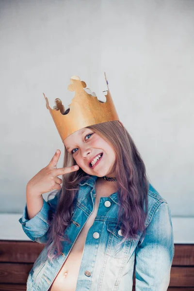 Porträtt av skolflicka med färgat hår bär gyllene krona, visar seger finger tecken och göra roliga ansikten. — Stockfoto