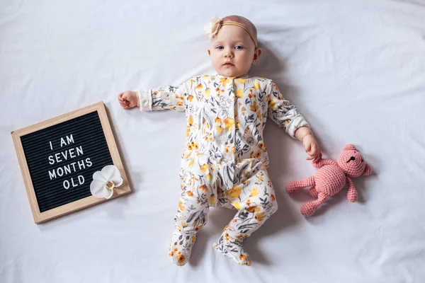 7 Sete meses de idade menina deitado no fundo branco com carta bordo e ursinho de pelúcia. Composição plana . — Fotografia de Stock