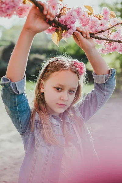 満開の桜の中にポーズをとる可愛い女の子の本物の肖像画. — ストック写真