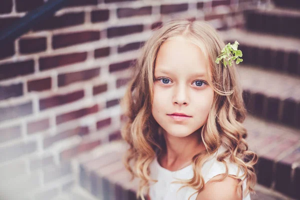 Nahaufnahme Porträt des schönen 9-10 jährigen Mädchens mit blonden lockigen Haaren, das auf der Treppe sitzt. — Stockfoto