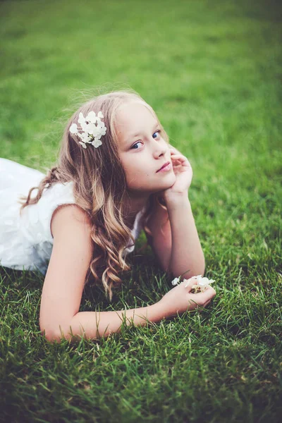 Outdoor portret van tiener kind meisje dragen witte jurk en liggend op het gras. — Stockfoto
