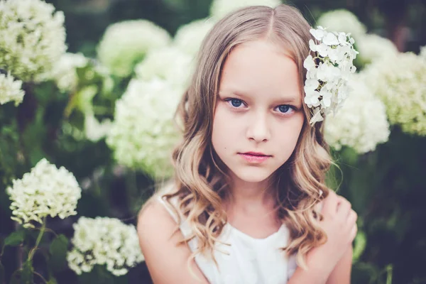 Fashion close-up portret van mooie 9 -10 jaar oud meisje poseren tegen bloeiende witte hortensia bloemen. — Stockfoto
