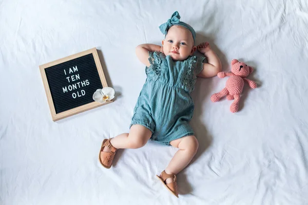 10 aylık bir bebek, beyaz arka planda, mektup tahtası ve oyuncak ayıyla yatıyor. Düz konum. Telifsiz Stok Fotoğraflar