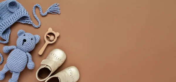 Flat lay banner with baby accessories set: crib shoes, teddy bear toy, knitted hat, wooden rattle and copy space.