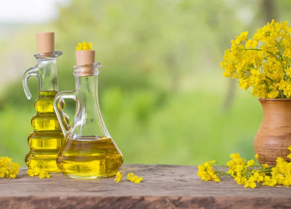 Rapsöl (Raps) und Rapsblüten auf Holztisch — Stockfoto