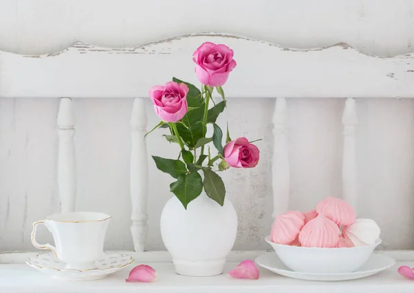 Pinc roses in vase and dinnerware on white wooden shelf — Stock Photo, Image