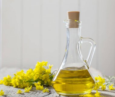 rapeseed oil (canola) and rape flowers on wooden table clipart