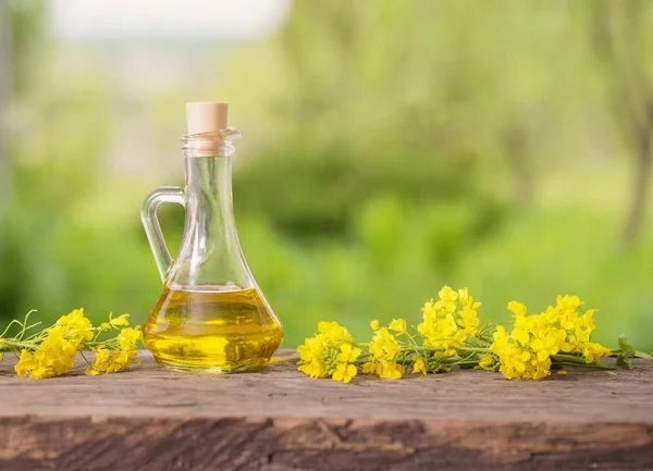 Rapsöl (Raps) und Rapsblüten auf Holztisch — Stockfoto