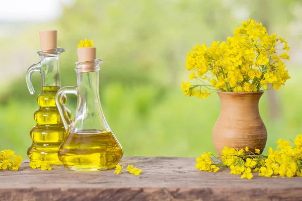 Rapeseed oil (canola) and rape flowers on wooden table — Stock Photo, Image