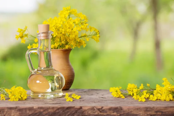 Rapsöl (Raps) und Rapsblüten auf Holztisch — Stockfoto