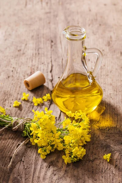 Olej rzepakowy (rzepakowy) i kwiaty rzepaku na drewnianym stole — Zdjęcie stockowe