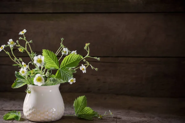 Bloemen van aardbei in vaas op oude achtergrond — Stockfoto