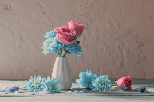 Flores azules y rosas en jarrón sobre fondo grunge blanco — Foto de Stock