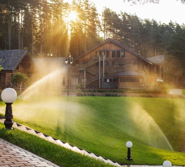 Arroser la pelouse près de la maison en bois un matin d'été — Photo