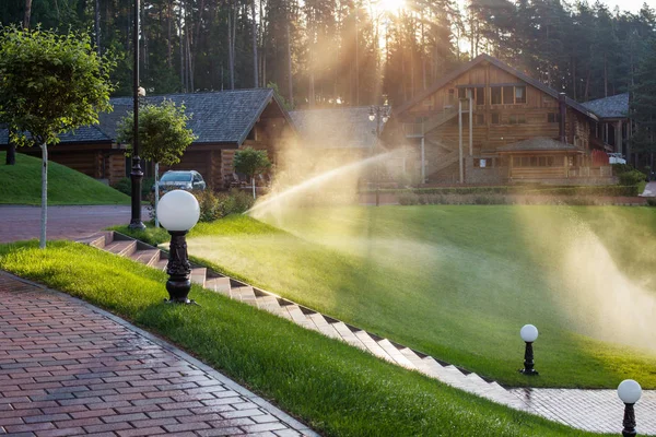 Bewässerung des Rasens in der Nähe von Holzhaus an einem Sommermorgen — Stockfoto