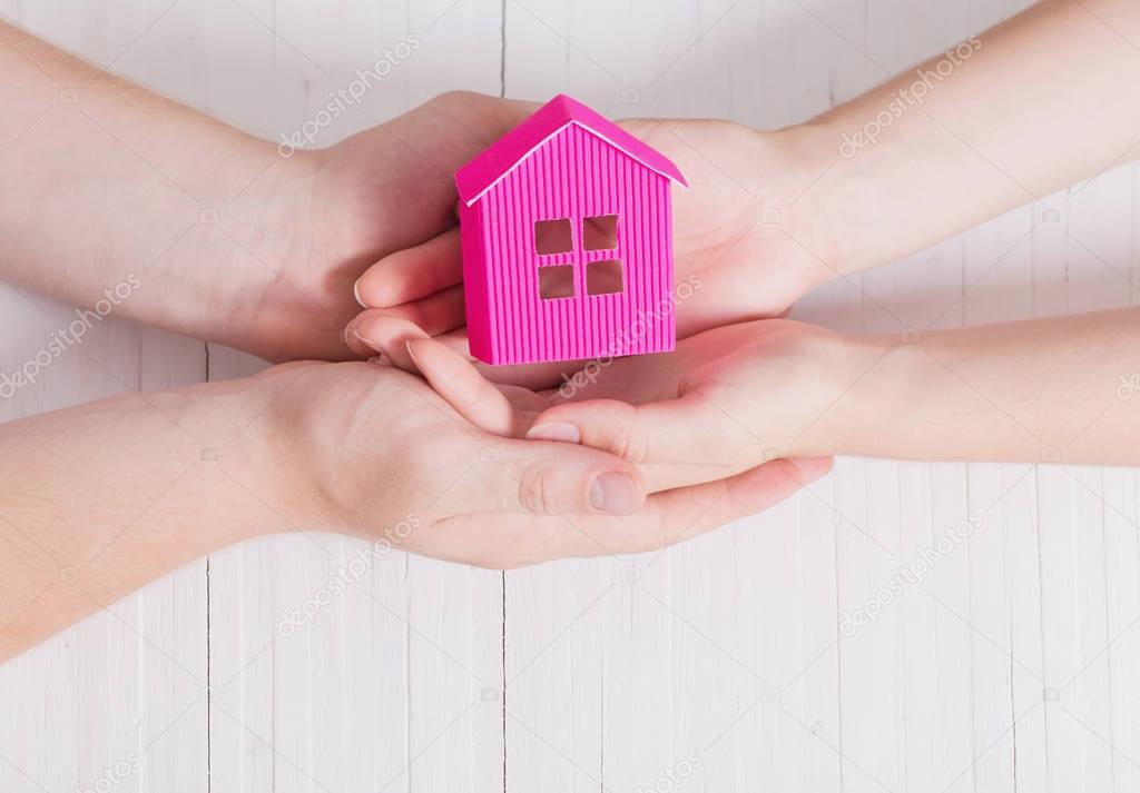 hands and paper house on white wooden background