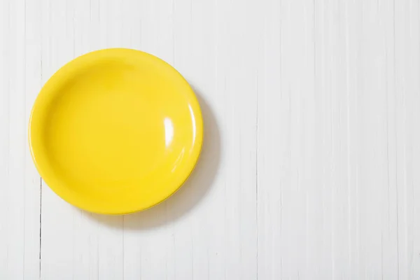 Yellow plate on white wooden background — Stock Photo, Image