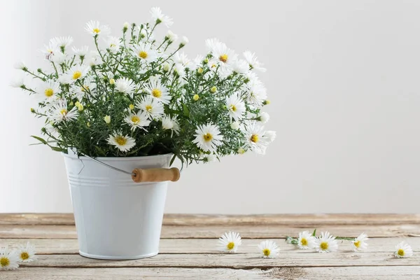 Białe kwiaty na wiaderko na drewnianym stole — Zdjęcie stockowe