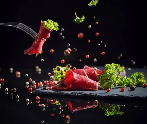 Carne fatiada com verduras em um fundo preto — Fotografia de Stock